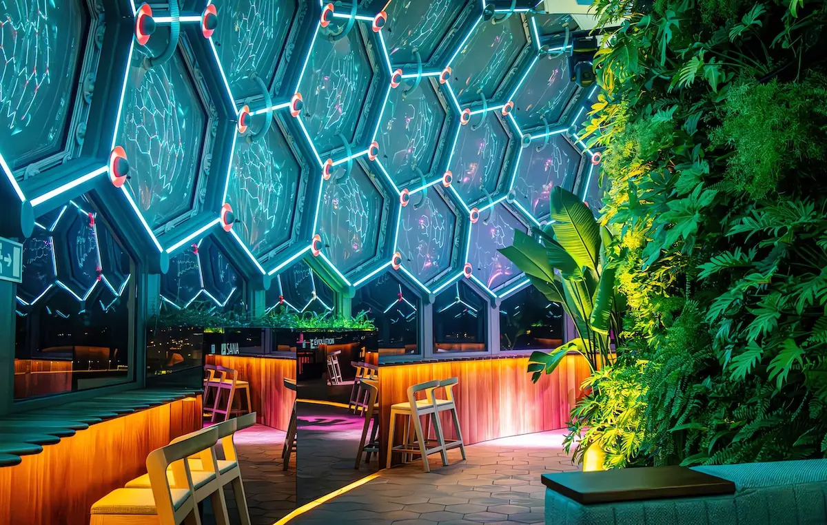 Interior do BABYLON 360 à noite: teto de painéis hexagonais contornados a néon azul, sobre uma parede verde iluminada.
